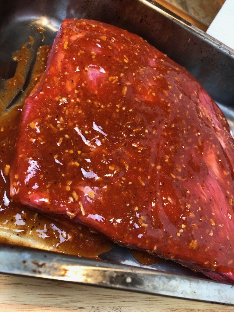 Brisket in a large roasting pan covered in Sauce