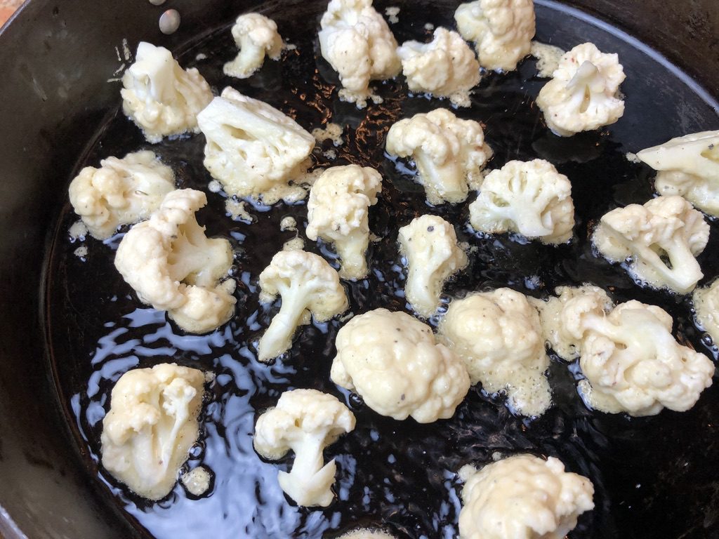 battered cauliflower florets cooking in the pan