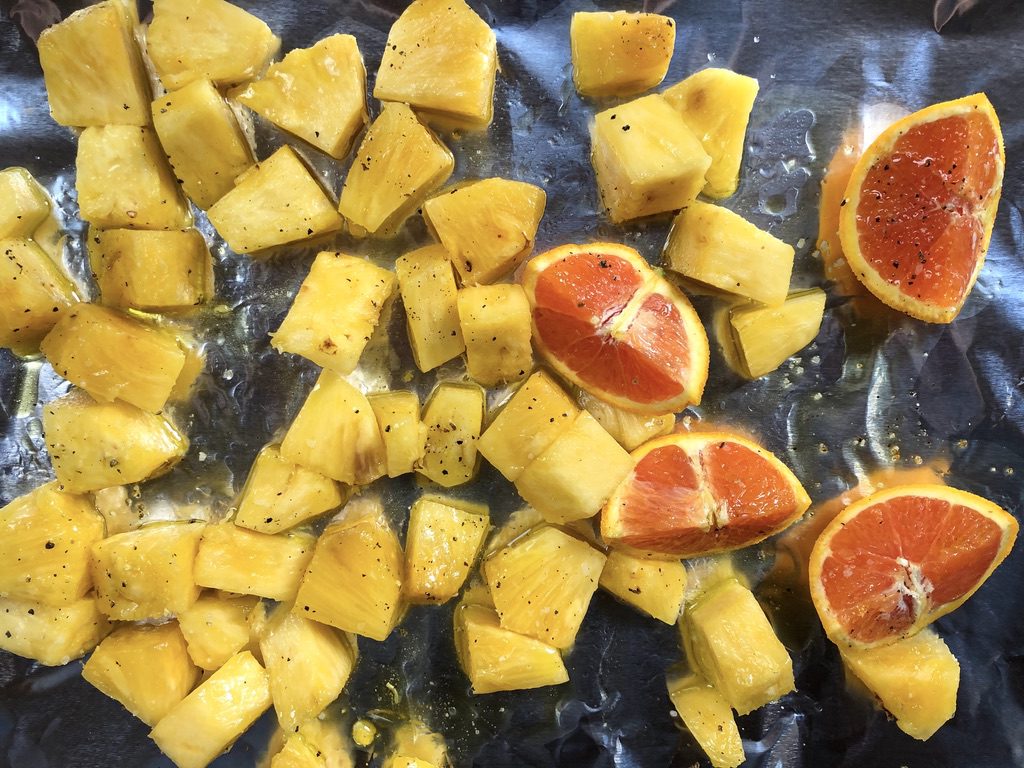 pineapple and orange on foil-lined tray with olive oil, salt, and pepper