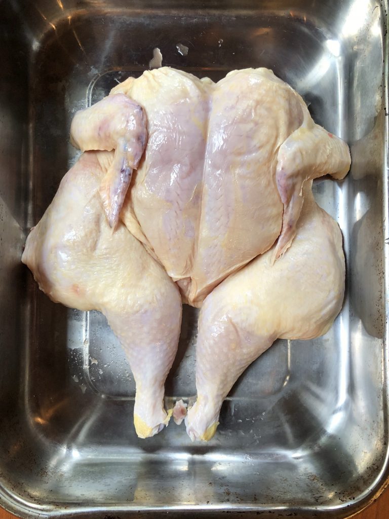 raw spatchcocked chicken in a baking dish