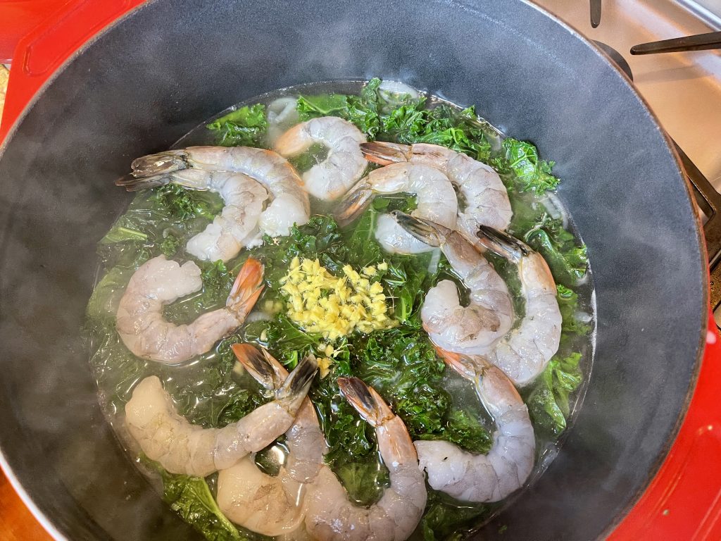 adding the ginger and shrimp to the wilted greens