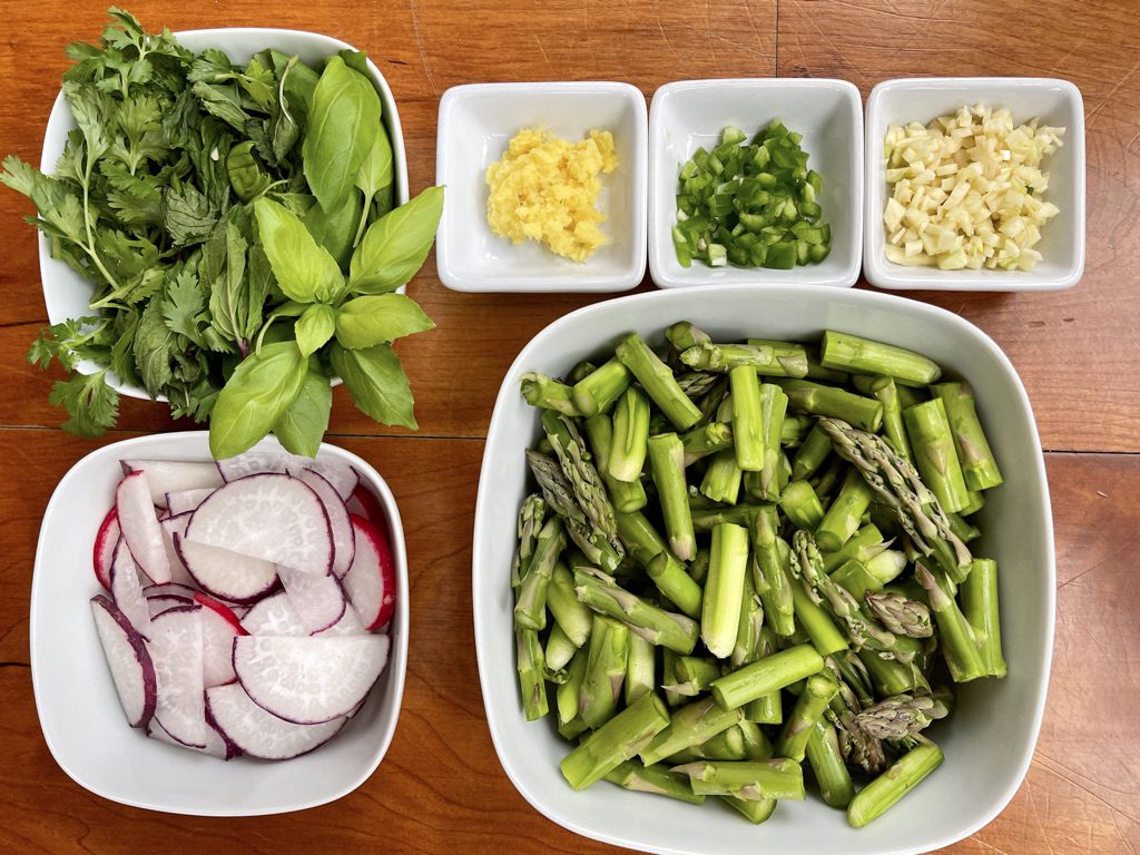 all ingredients for the recipe: asparagus, radishes, ginger, garlic, chiles, and fresh herbs (mint, basil, cilantro).