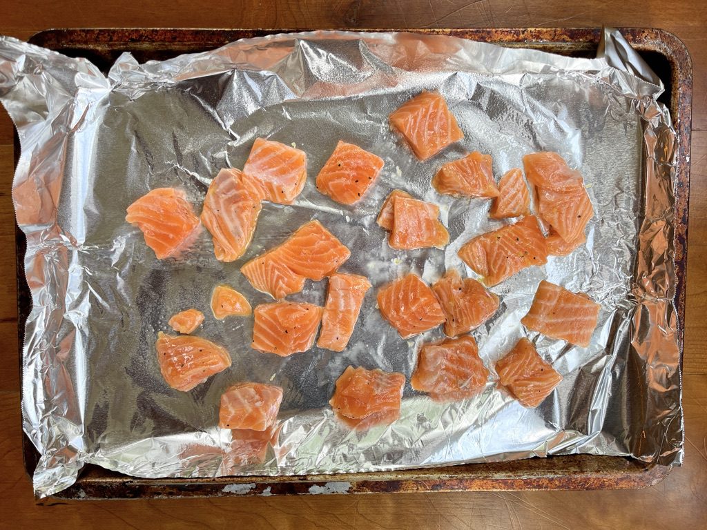 salmon chunks coated in lemon zest oil on a foil-lined baking sheet