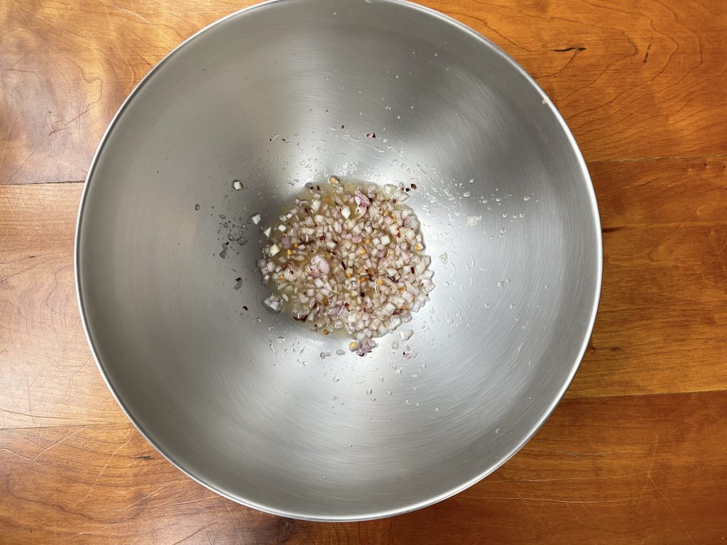 mixing the dressing base ingredients together in a large bowl - lemon, shallots, salt, hot pepper flakes and honey