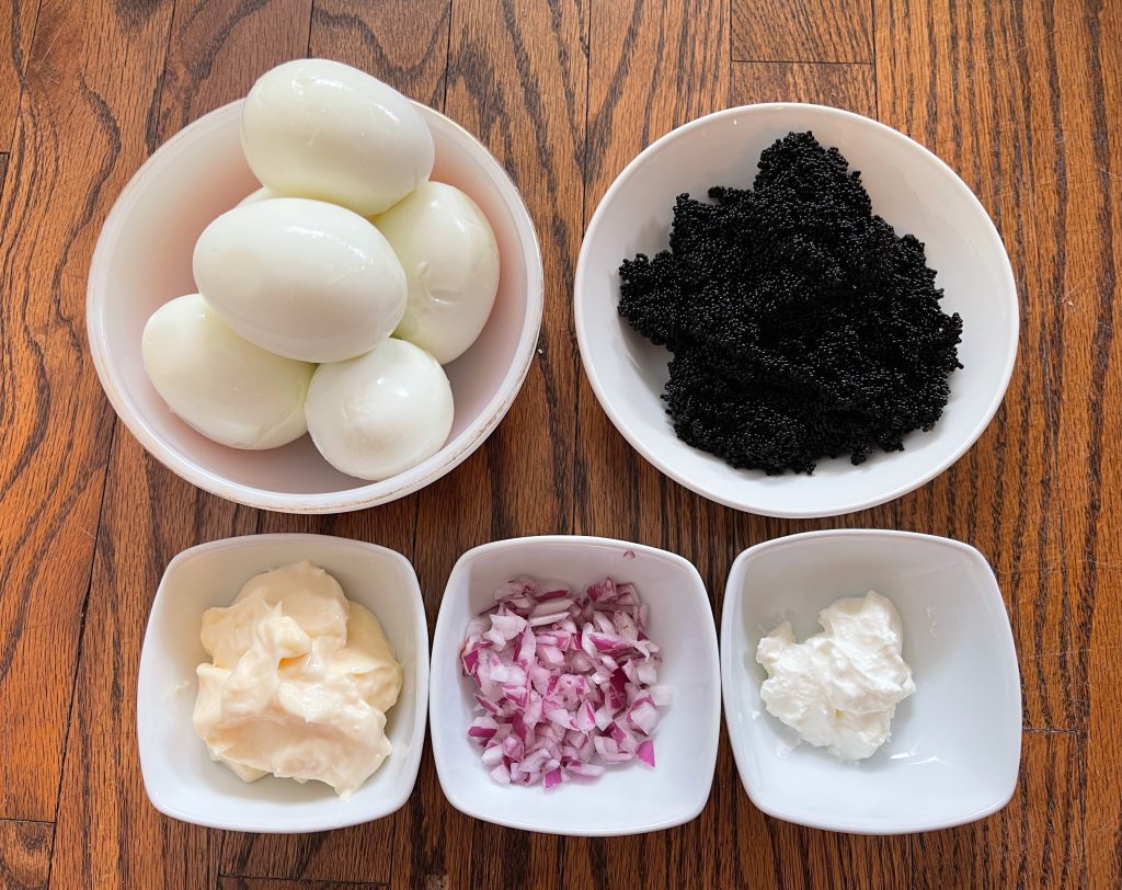 ingredients for vintage caviar pie - hard boiled eggs, chopped onion, mayo, sour cream, and black tobiko/caviar