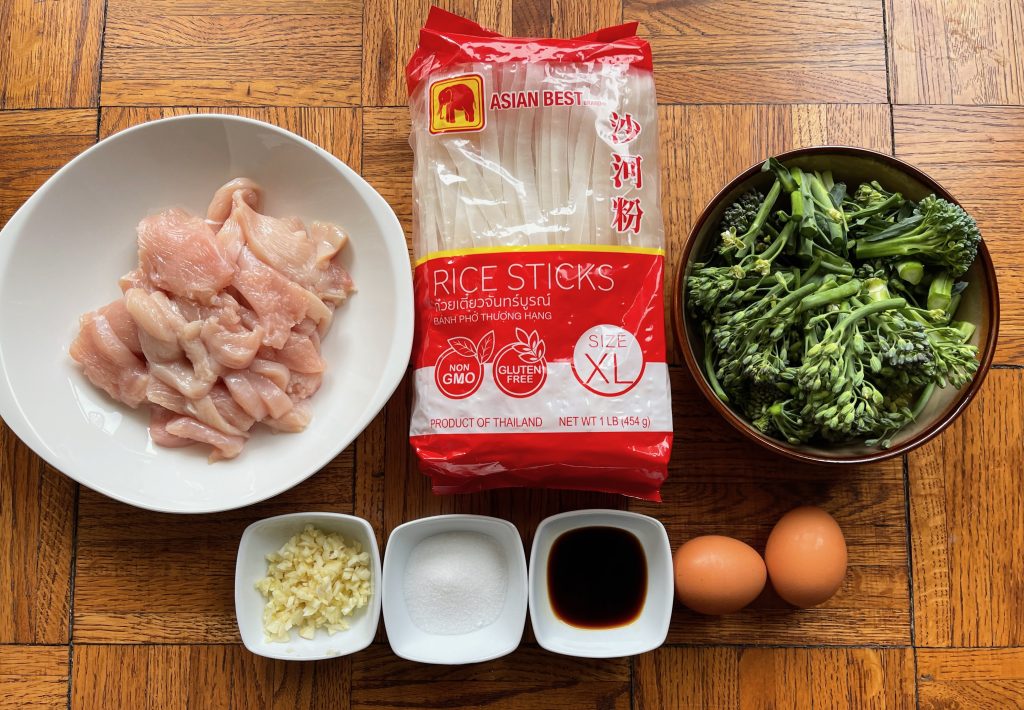 ingredients for pad see ew - thinly sliced chicken, wide rice noodles, broccolini spears cut into quarters, two eggs, garlic, gf soy sauce, and sugar