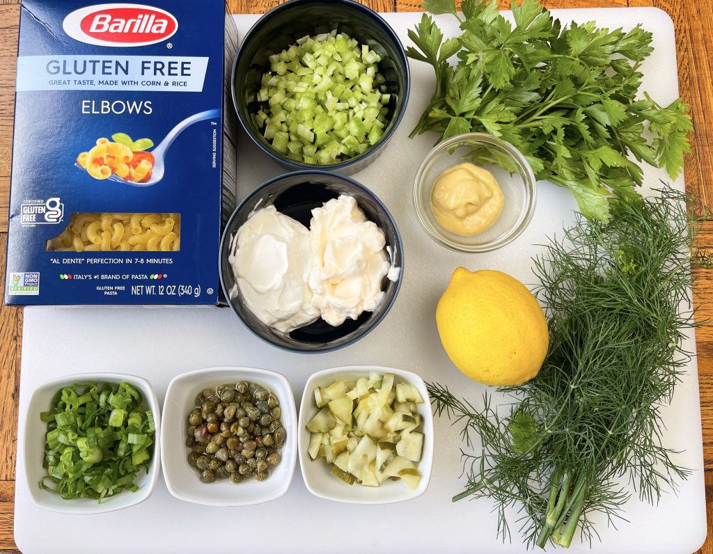 ingredients - gluten free elbow macaroni, dill, parsley, dill pickles, celery, capers, scallions, lemon, mayo, sour cream, dijon mustard, and sugar (not photographed)