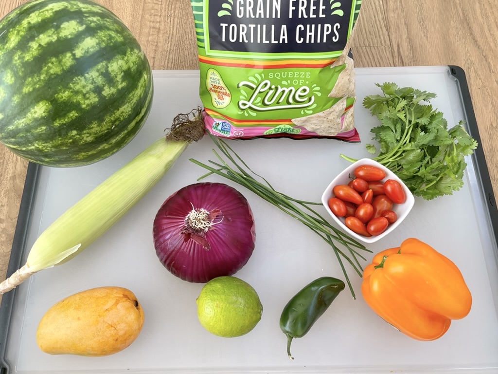 Summer Salsa ingredients - watermelon, mango, corn, red onion, tomatoes, orange pepper, cilantro, chives/scallions, lime, gluten free chips