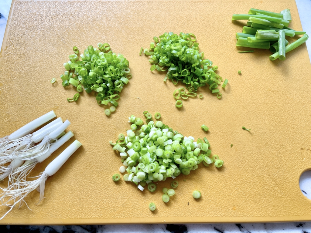 trimming tops off scallions and then slicing and dividing into dark, pale green, and white piles