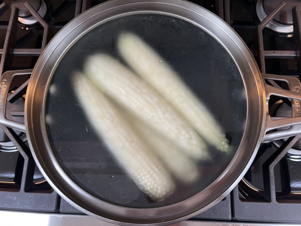 Place husked corn in large pot of boiling water. Lower heat to a soft boil and place lid on the pot. Set timer for 5 minutes.