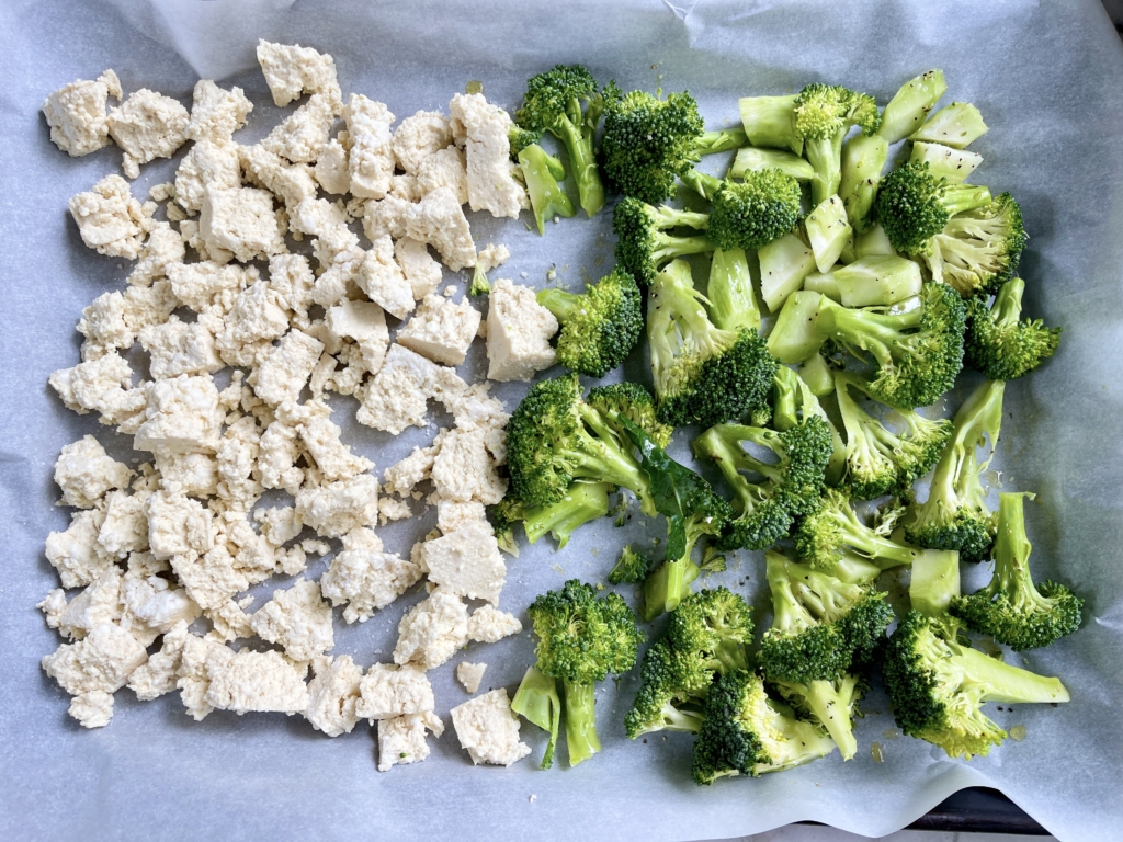 Place parchment paper on a baking sheet and put broccoli florets on one half of the tray and the tofu on the other half. Season both with salt and olive oil and mix each half so that they are coated.