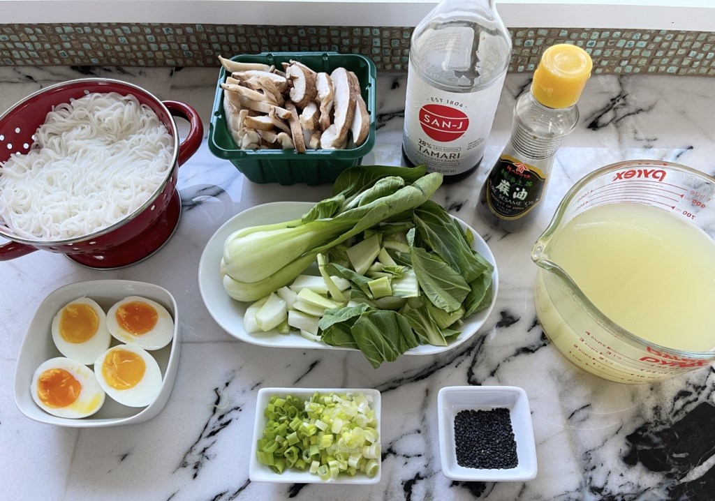 Organize the ingredients - sesame oil, scallions, shiitakes, bok choy, broth, gluten free soy sauce, cooked rice vermicelli noodles, cooked jammy eggs, and black sesame seeds (optional)