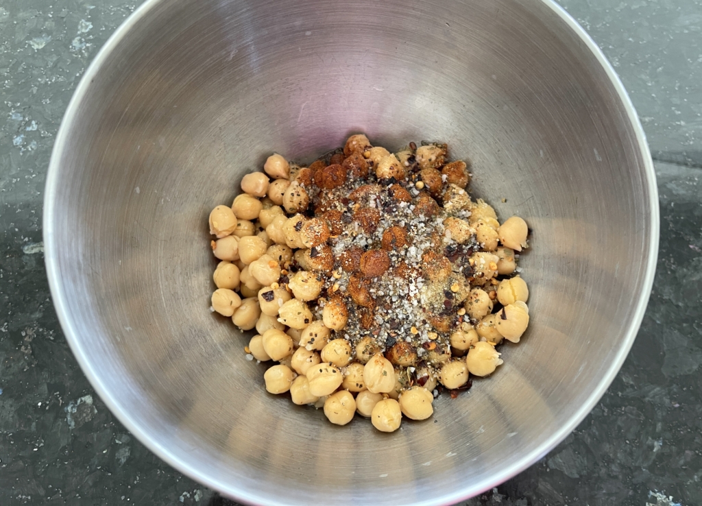 Drain and rinse the garbanzo beans and place them in a large bowl. Add 2 tablespoons of olive oil and the spices - dried oregano, paprika, garlic powder, red pepper flakes and salt.