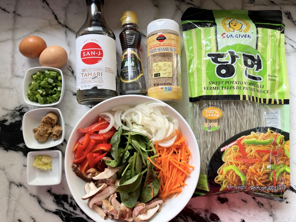 ingredients - korean sweet potato rice vermicelli noodles, eggs, red pepper, carrots, onions, shiitakes, spinach, scallions, dark brown sugar, garlic, gluten free soy sauce, sesame oil, black pepper, and sesame seeds.