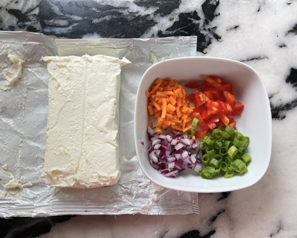 Allow one block of cream cheese to come to room temperature, and dice red pepper, red onion, carrot, and scallions