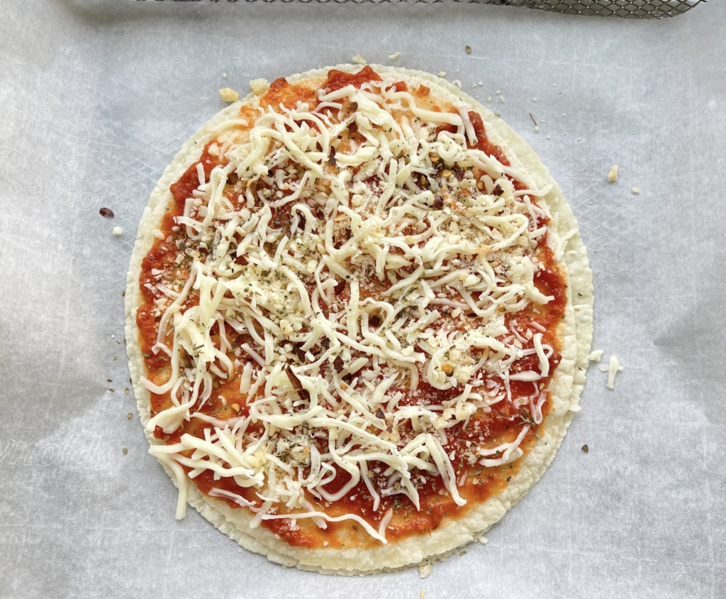 Scatter the remaining 2 heaping tablespoons of shredded mozzarella cheese and 2 teaspoons grated parmesan cheese on top of the sauce. Finish off your Tort-izza with seasonings such as oregano and hot pepper flakes, if desired. 