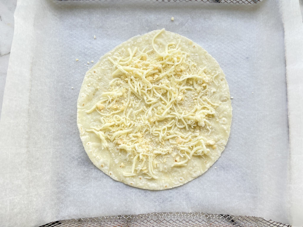 Place first tortilla on a flat surface and scatter 2 heaping tablespoons of shredded mozzarella cheese and 2 teaspoons grated parmesan cheese on the tortilla.