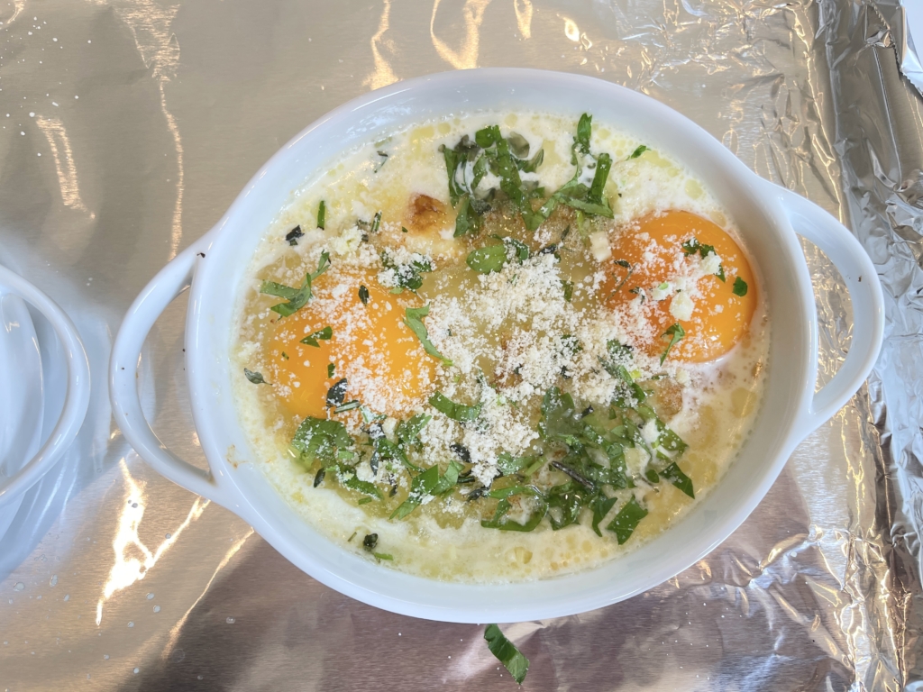 While the broiler is heating up, combine the garlic, thyme, rosemary, parsley, and Parmesan in a small bowl and set aside. Remove the tray from oven and quickly and carefully, pour the 2 eggs into each gratin dish and sprinkle evenly with the herb mixture. 