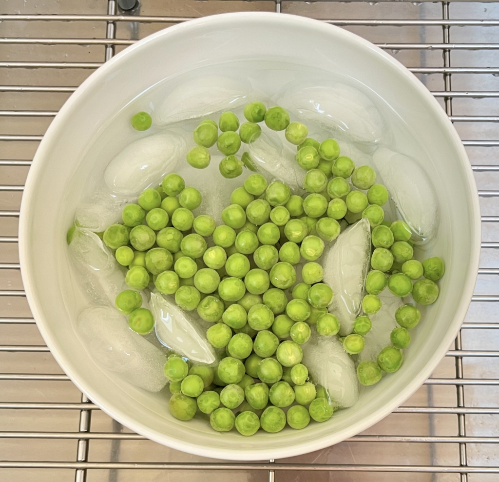 Then immediately transfer peas to a medium sized bowl of water with ice cubes. This will lock in the vibrant green color of the peas. After 1 minute of the ice bath, drain peas again and set peas aside.