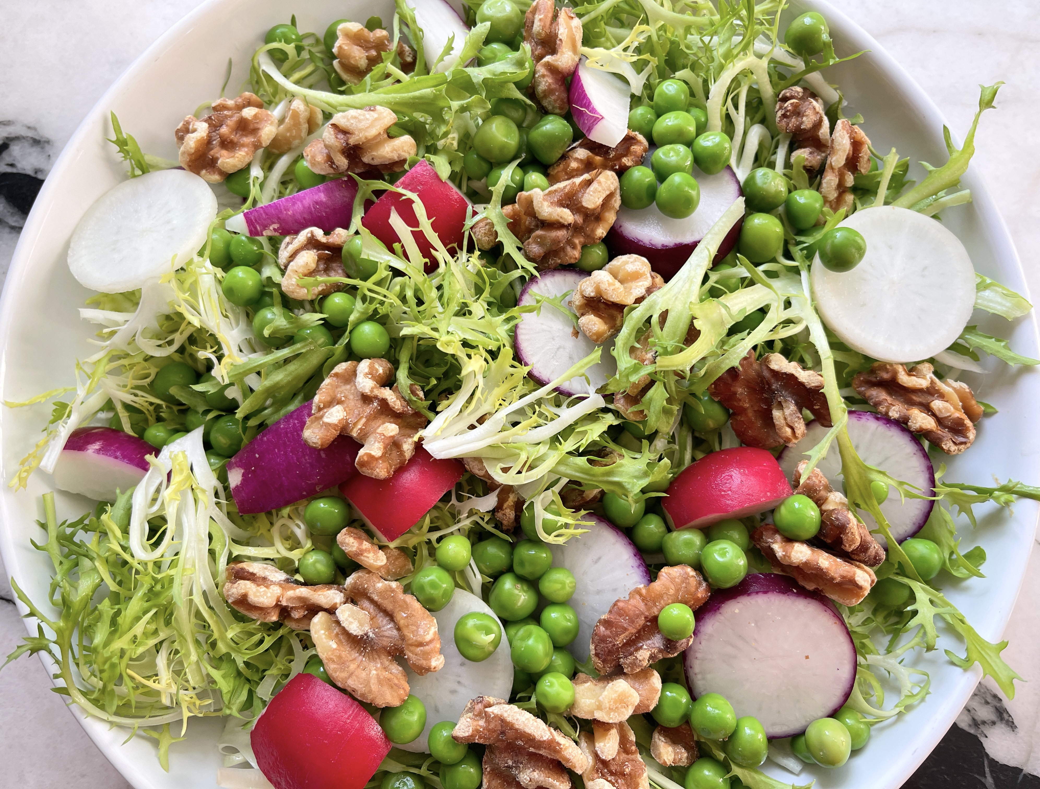 Layer the frisée, peas, radishes, and walnuts in a shallow serving platter or a medium-sized bowl.