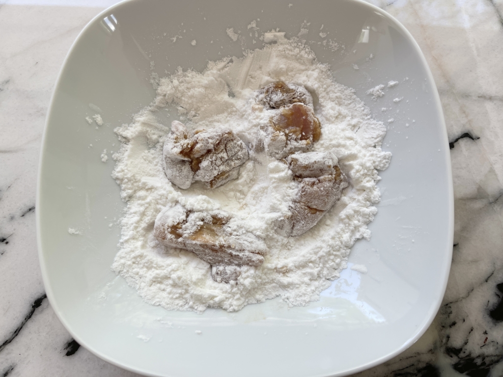 Place 4-5 chicken pieces into the potato starch mixture and cover pieces fully and then shake off any excess starch.